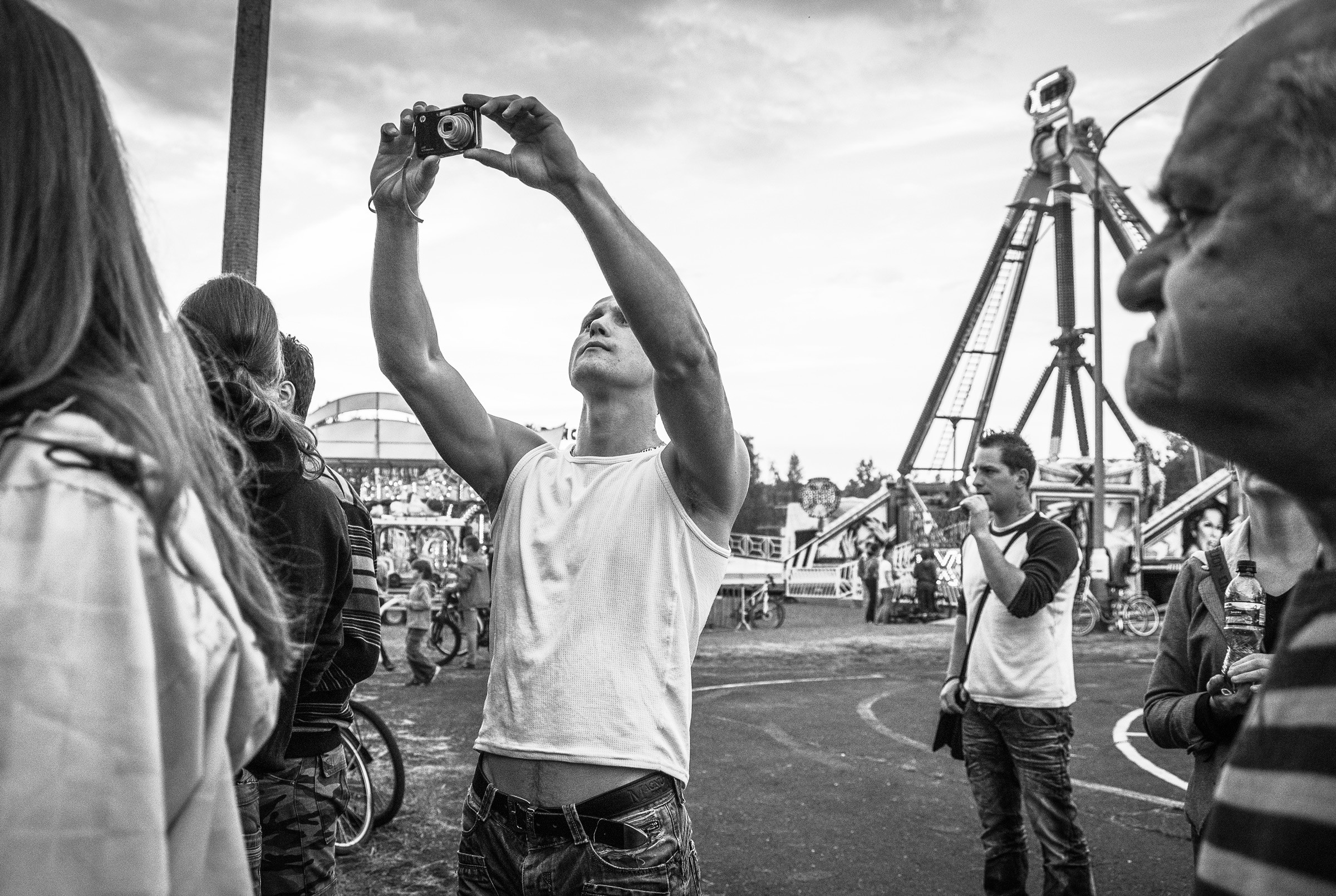 Czarno-biały kadr z festynu. Na pierwszym planie mężczyzna robiący zdjęcie.