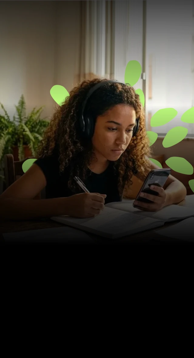 Mulher jovem estudando com um caderno e com o celular na sala de estar