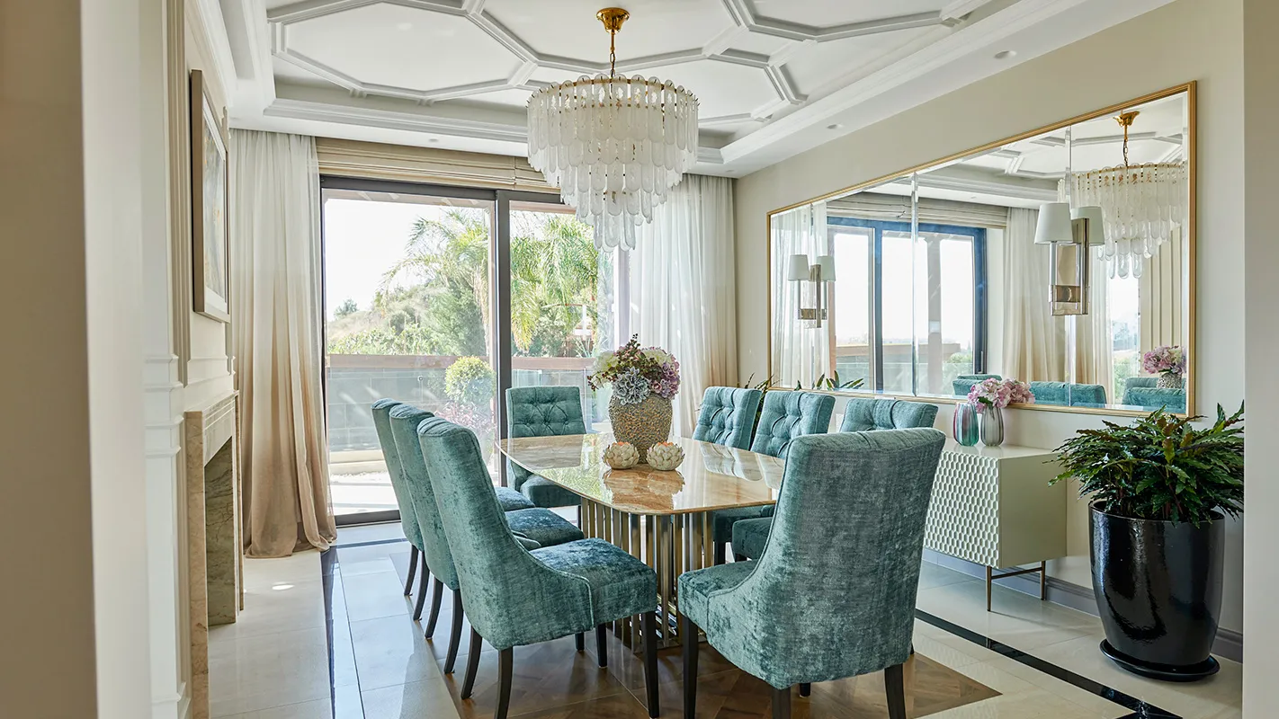 Villa Belmare dining room with turquoise upholstered chairs, crystal chandelier, and large wall mirror