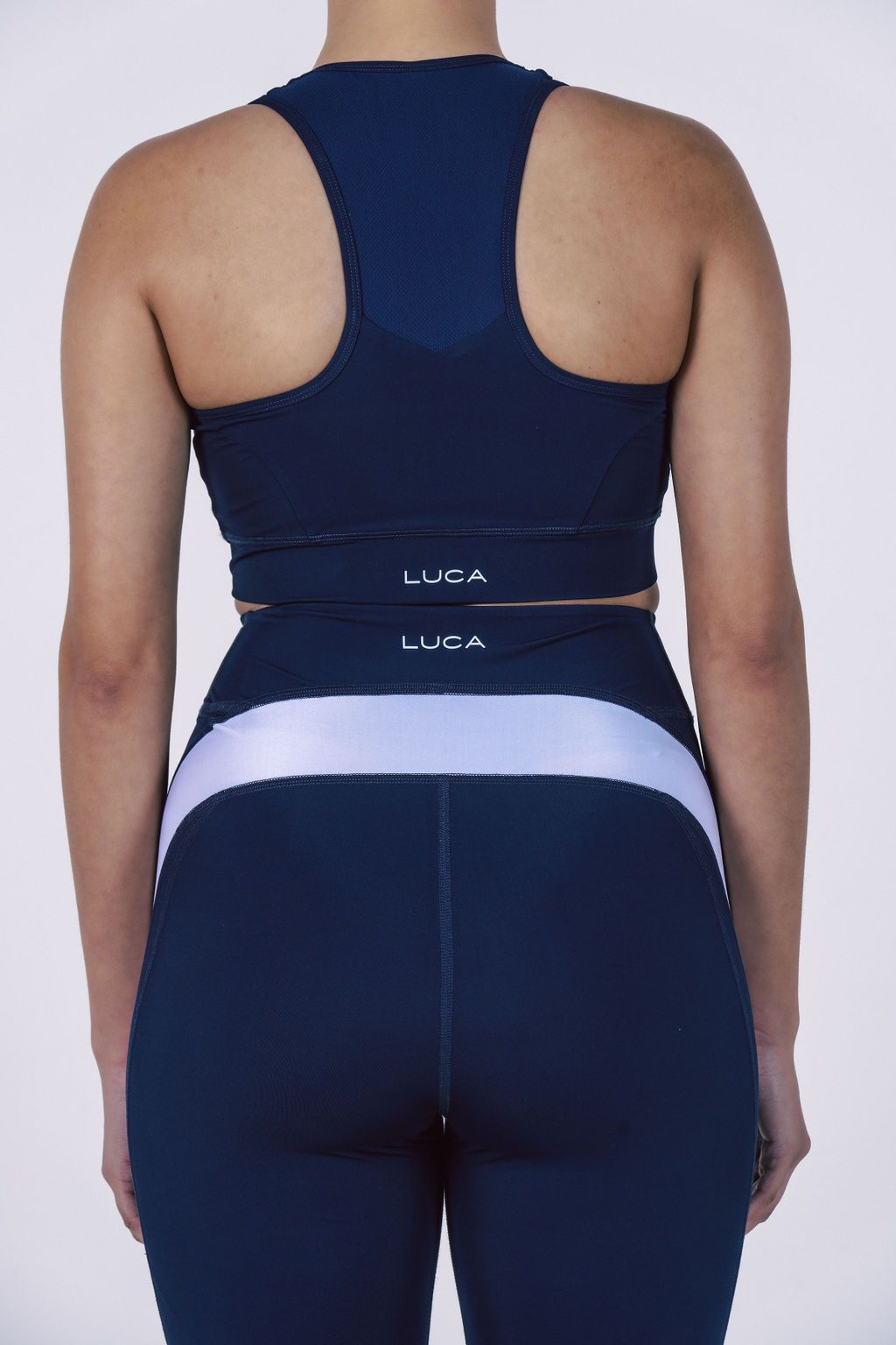 Rear-view-of-a-navy-blue-athletic- set-showing-a-racerback-sports-bra-and-compression-shorts-with-a- wide-horizontal-white-contrast-stripe-and-LUCA-branding