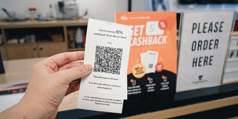Hand holding receipt featuring a cashback QR Code