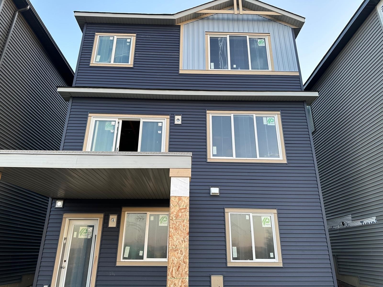 Three-storey new build with dark blue vinyl siding and light vertical accent panel