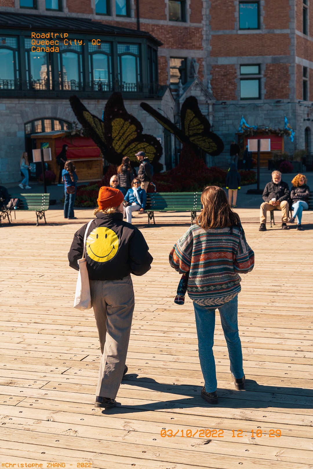 Scène urbaine à Québec avec deux amis de dos, des sculptures de papillons en arrière-plan.