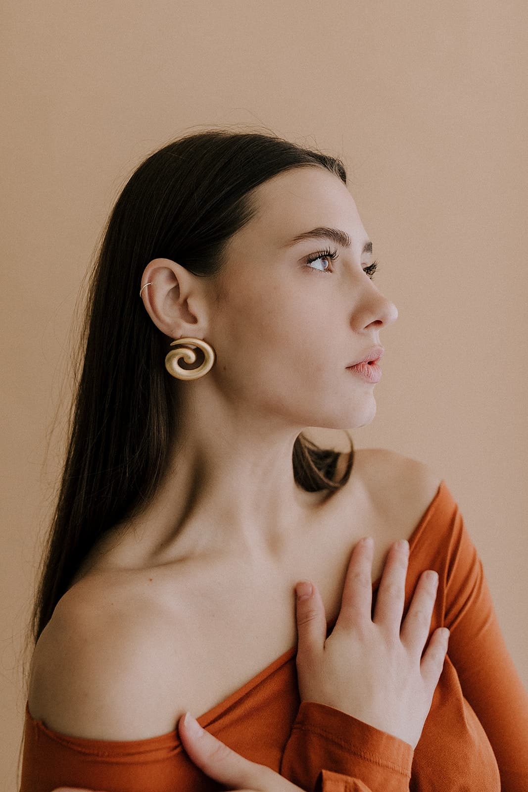 A profile view of a model wearing gold spiral earrings and holding her hand over her chest in a photography studio in Shreveport.