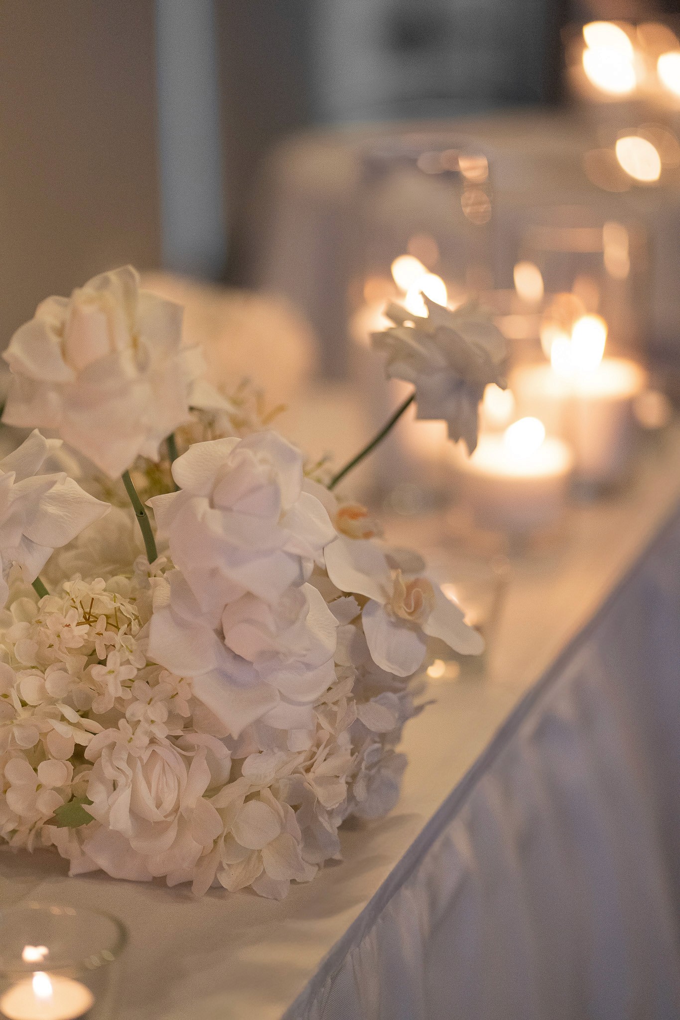 White floral arrangement and glowing candles along a wedding reception table.