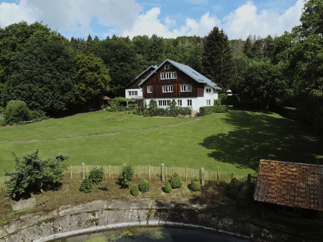 A cozy living room featuring a beige sofa with plush pillows and a furry throw, a modern rocking chair draped with a soft pink blanket, illuminated by warm light from a stylish floor lamp, set against a contrast of dark brown and white walls, with sheer curtains letting in natural light over a geometric patterned area rug.