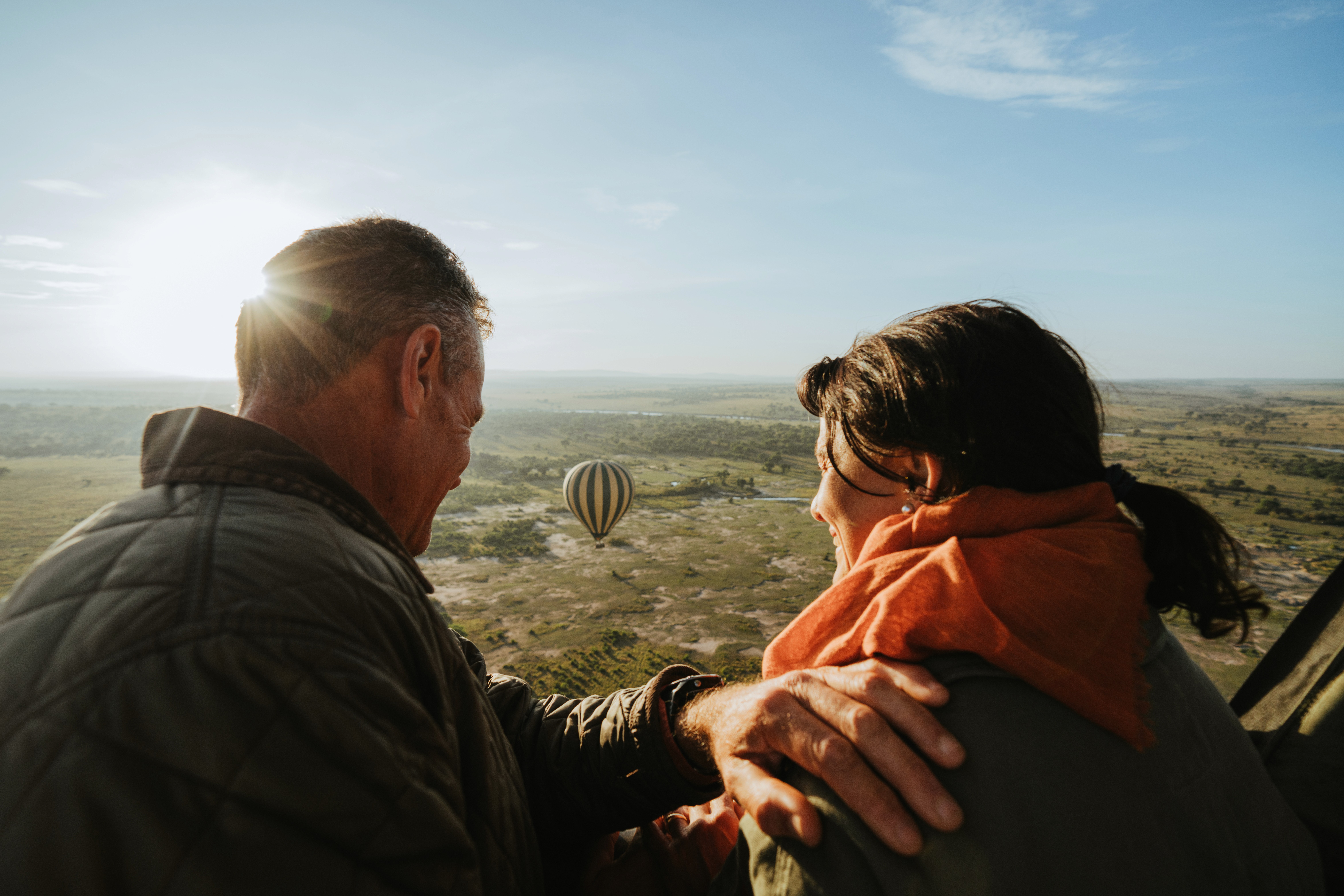 A couple watching another balloon drift over the plains from their basket