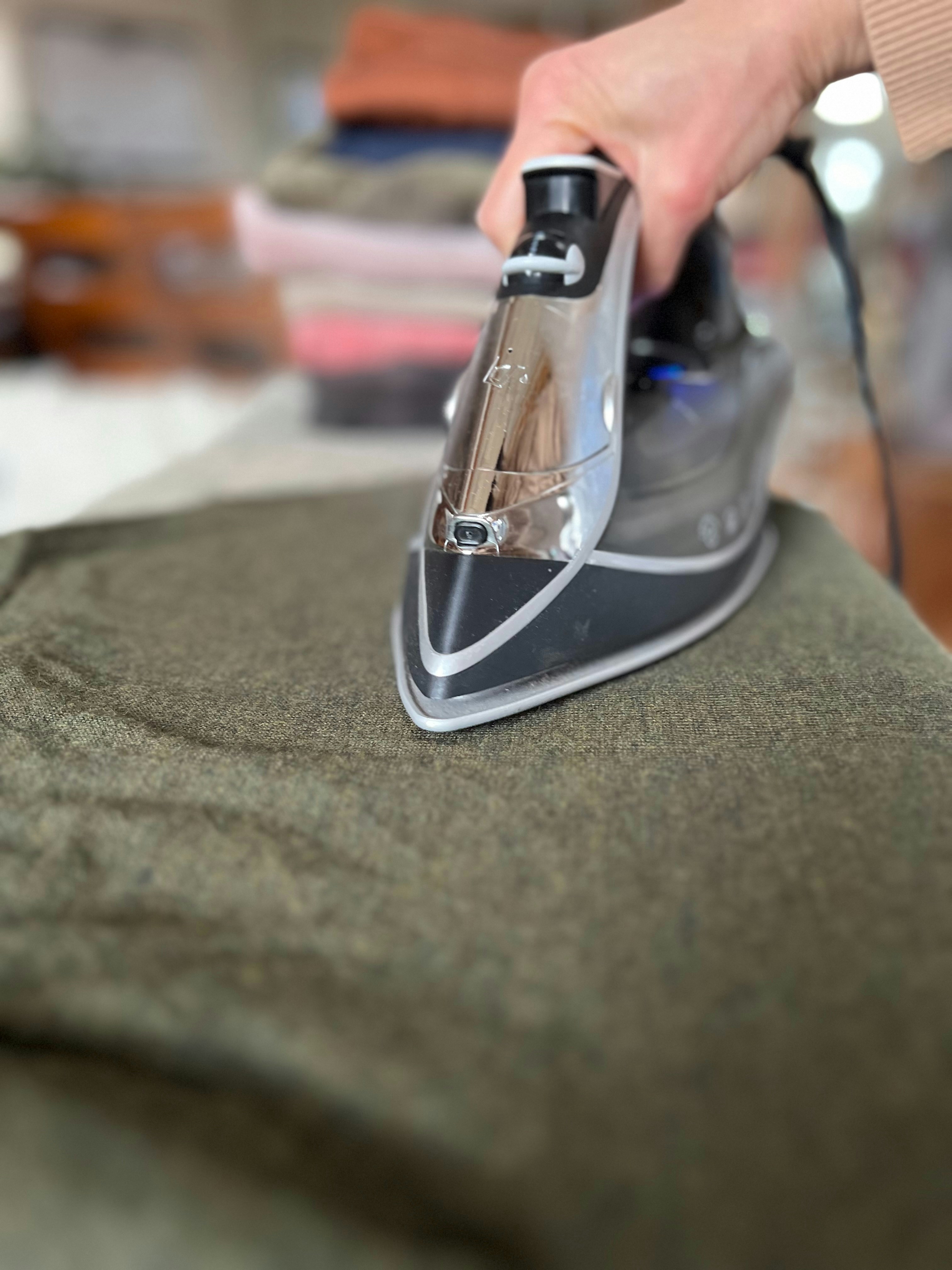A person ironing a green shirt with a black iron