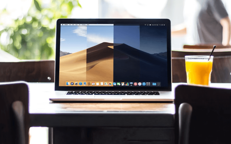 A macbook on a table with a glass of orange juice next to it.