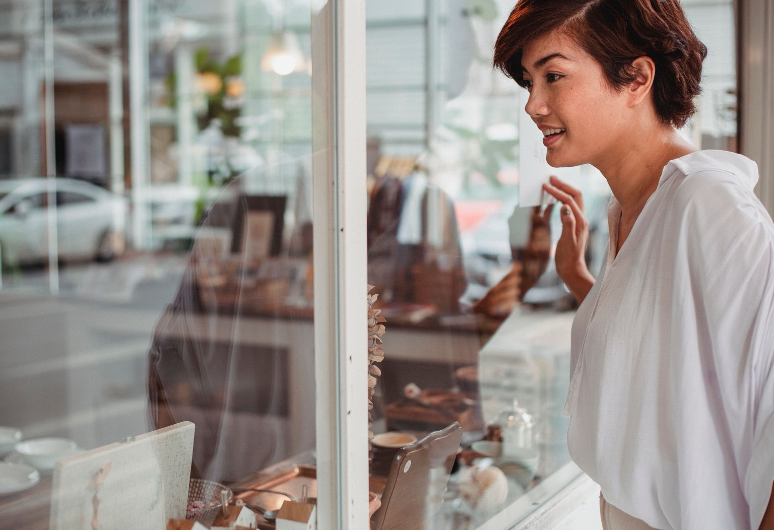 A woman pauses at a shop window and looks inside with curiosity.