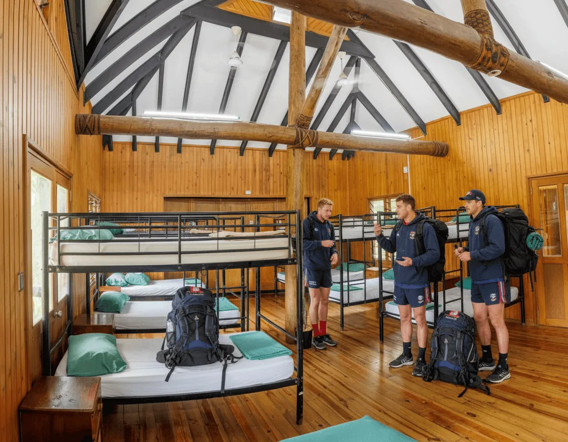 Sports team members with backpacks in a Uprising Beach Resort dormitory room with bunk beds.