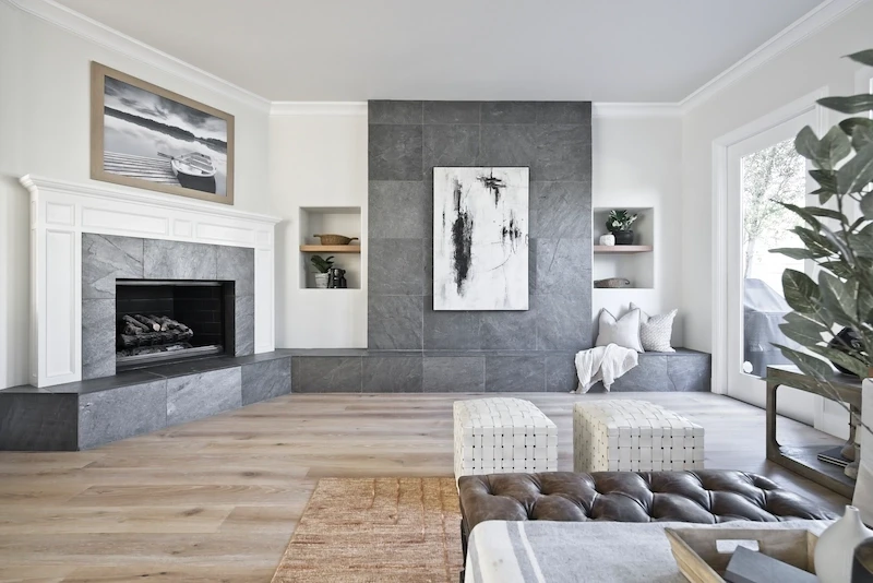 Living room with a sleek fireplace, gray accent wall, and white poufs in Bonita Canyon Remodel.