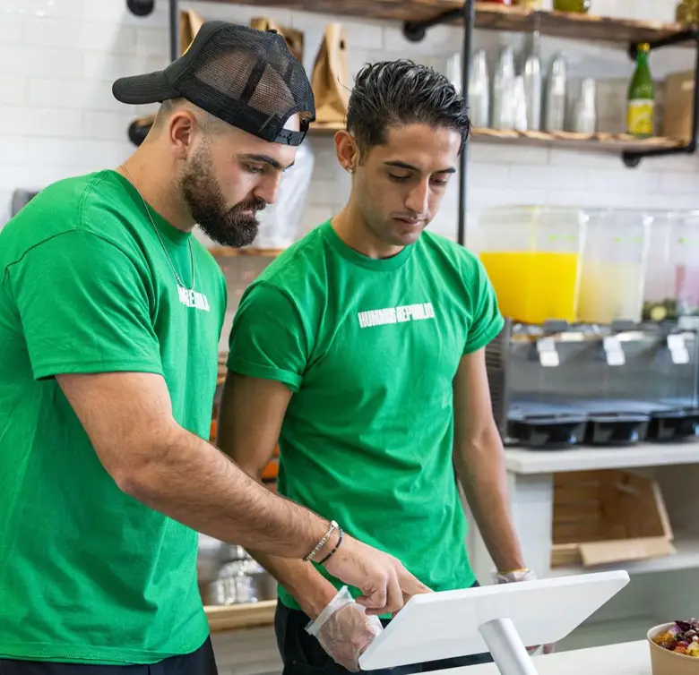 two employees behind the point of sale with green shirts on