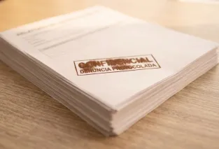 Pilha de documentos de papel sobre uma mesa, com um carimbo contendo a palavra "CONFIDENCIAL" marcado no topo.