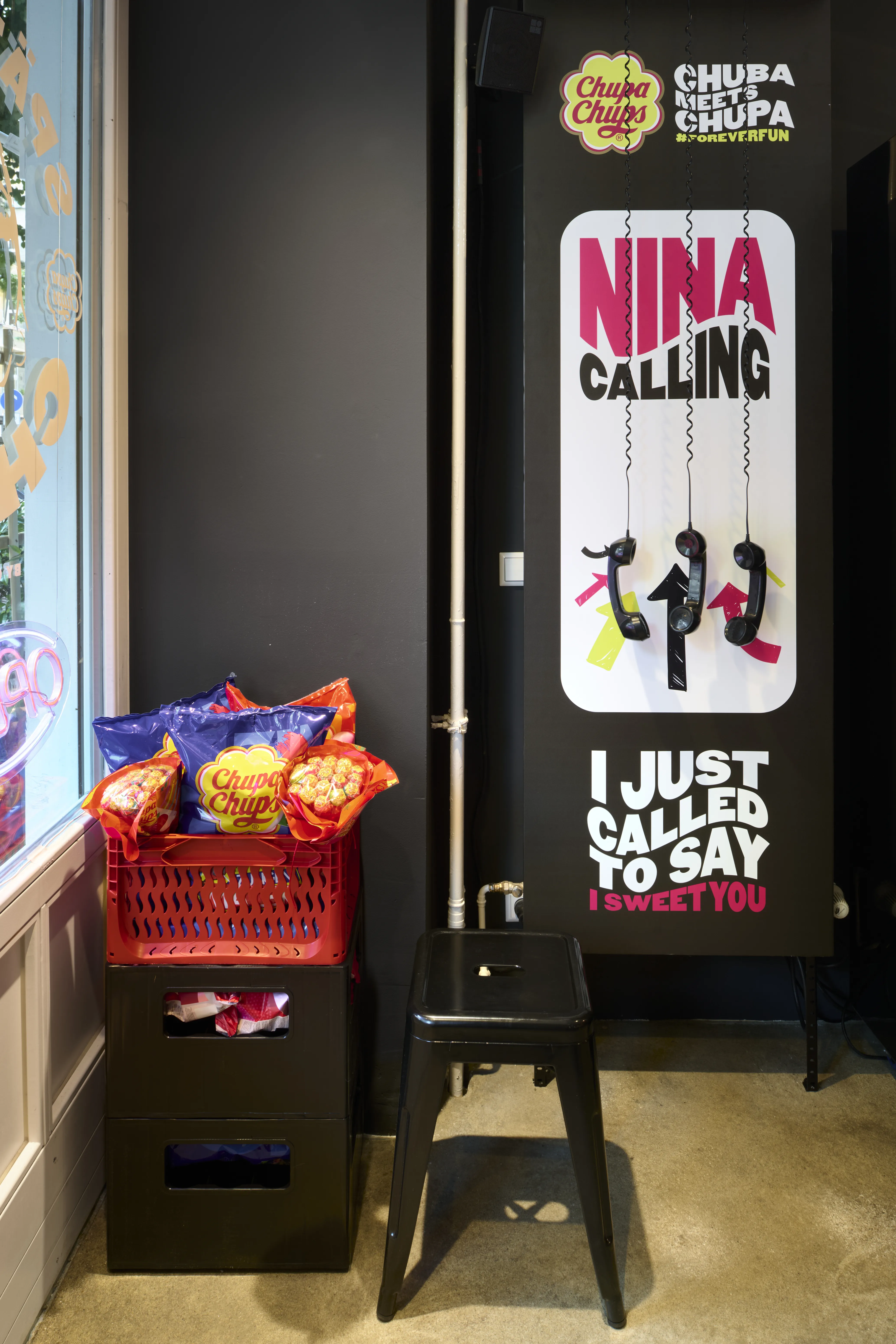 Nina Calling poster with dangling phone receivers next to a red basket of Chupa Chups bags in the pop-up kiosk.