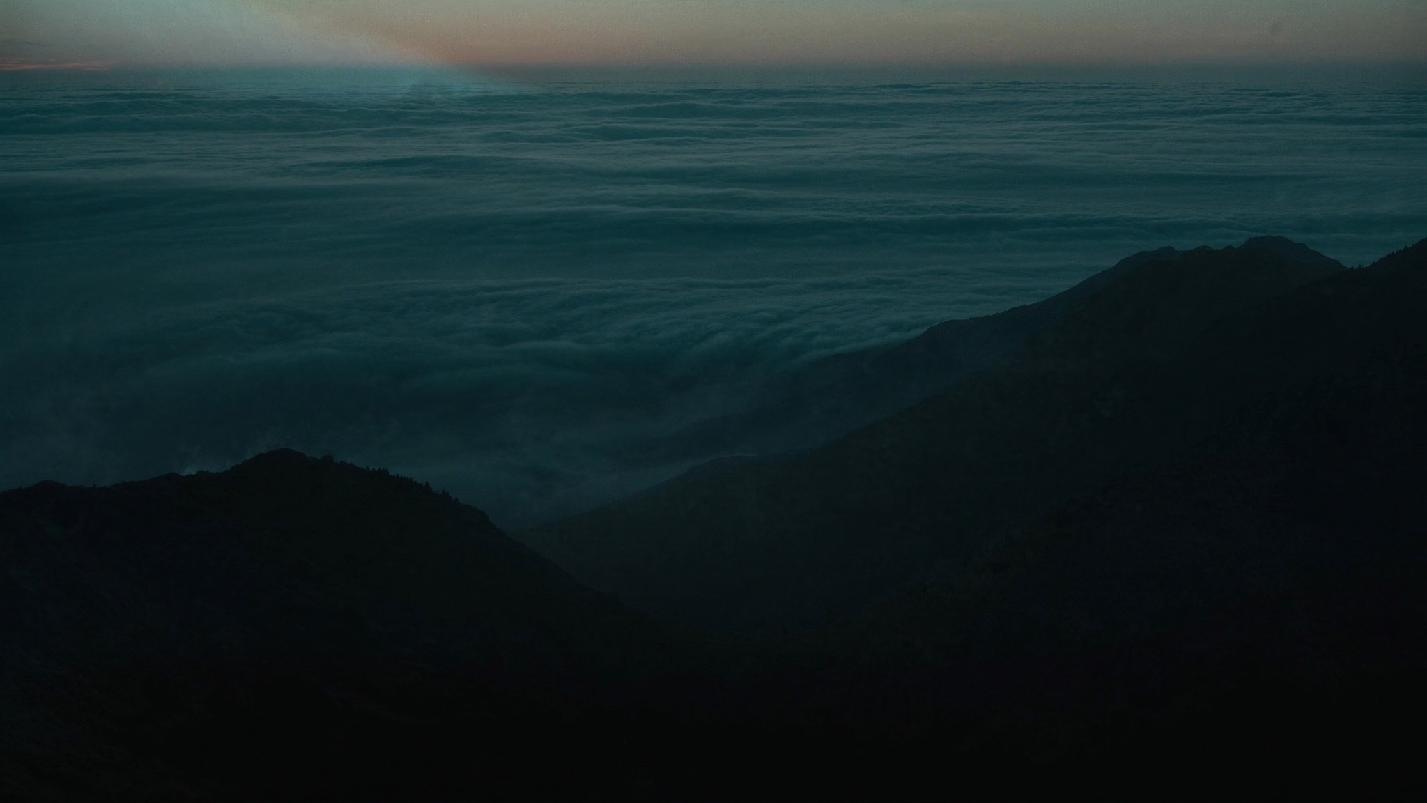 Sea of low cloud under a dark mountain ridge at dusk.