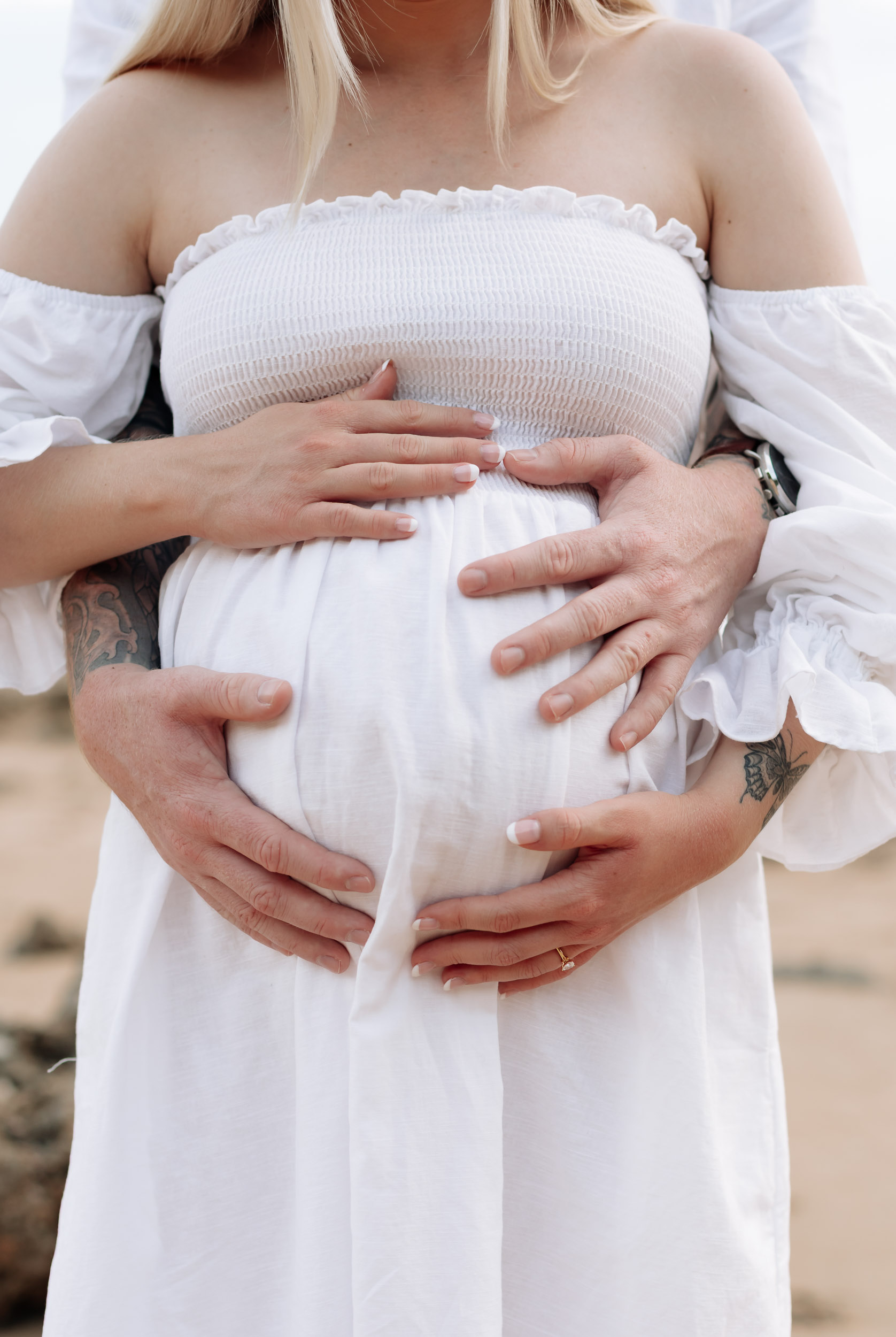 Couple embracing baby bump on the beach at sunset during a maternity session in Mackay Queensland