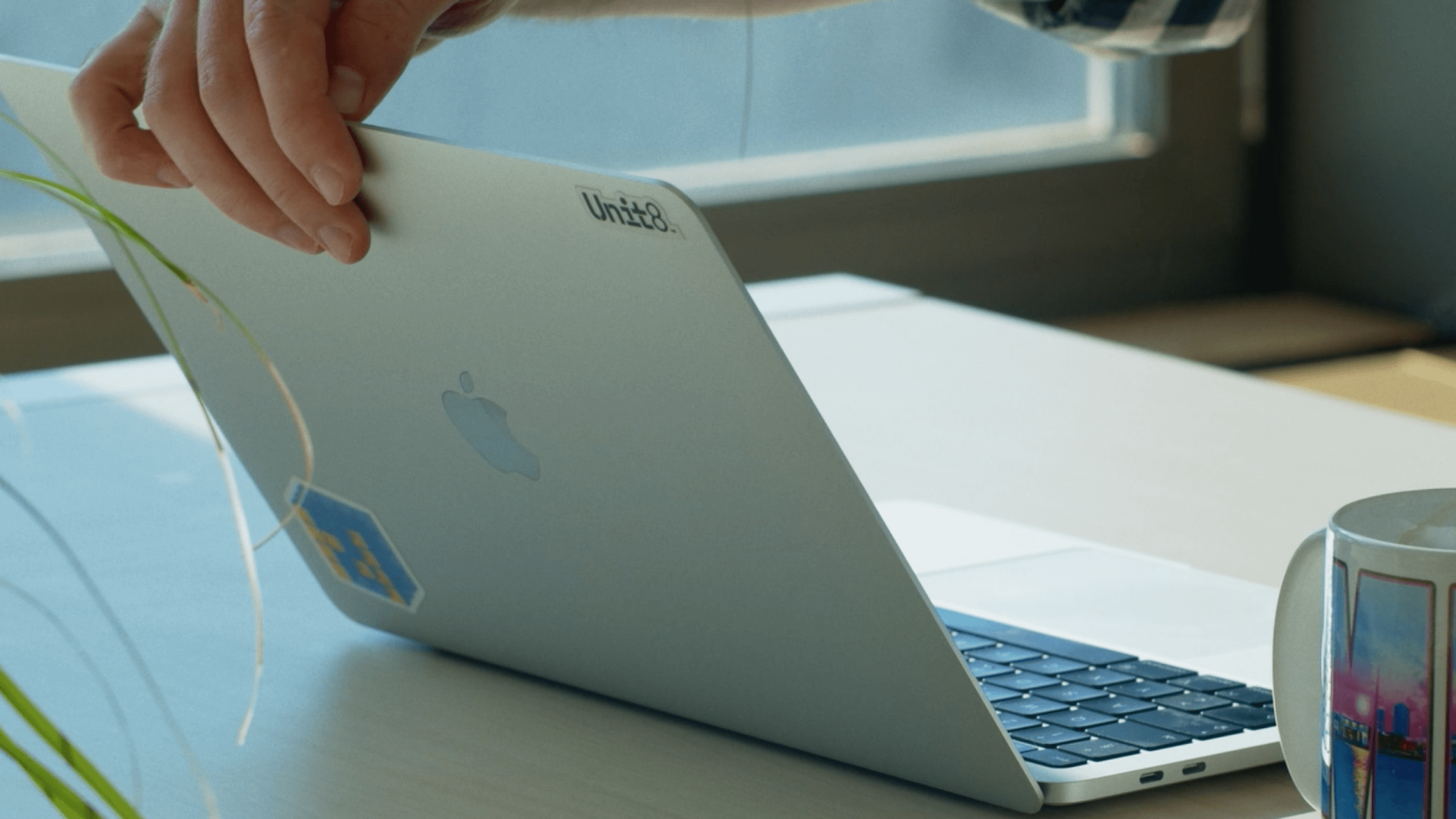 Laptop z naklejką Unit8 na klapie, na biurku przy oknie