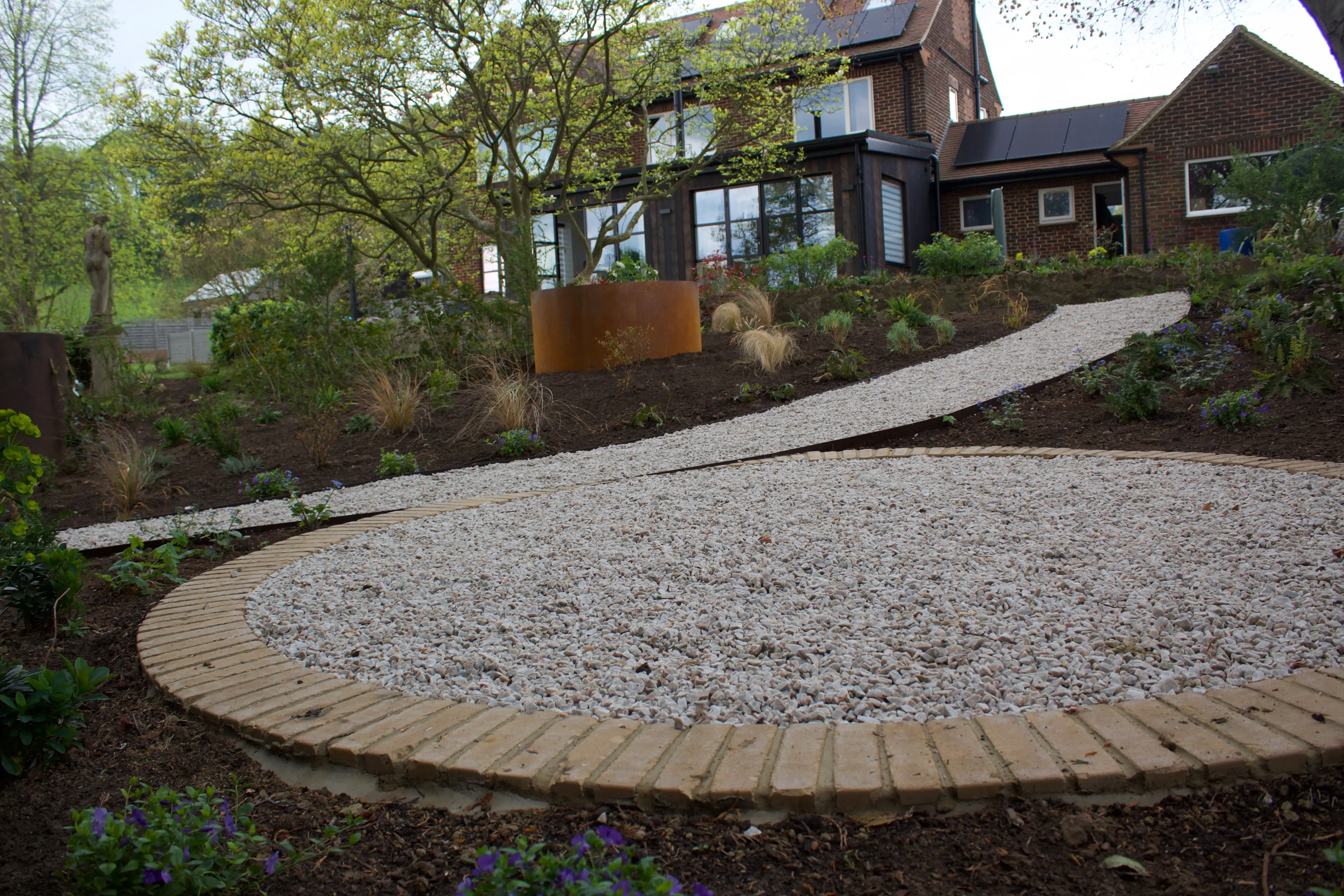 A curved stone path leads to a house surrounded by greenery and trees in a serene outdoor setting.