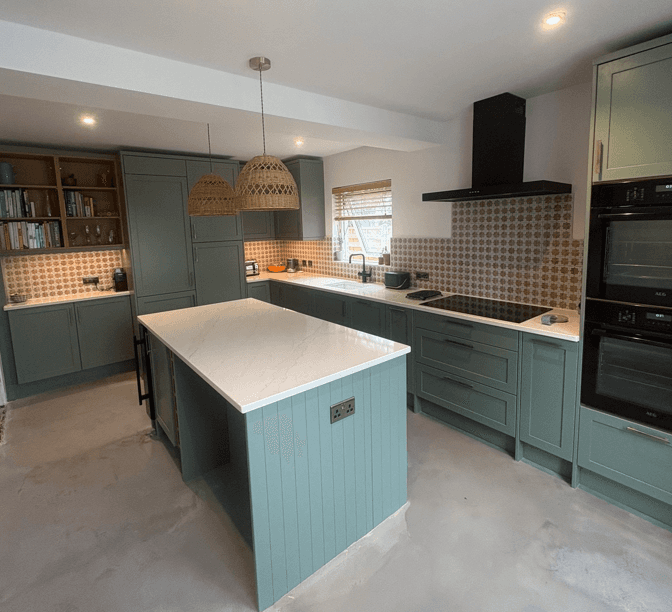 Kitchen with sage-green cabinets, a central island, pale worktops, patterned splashback tiles, woven pendant lights and built-in ovens.