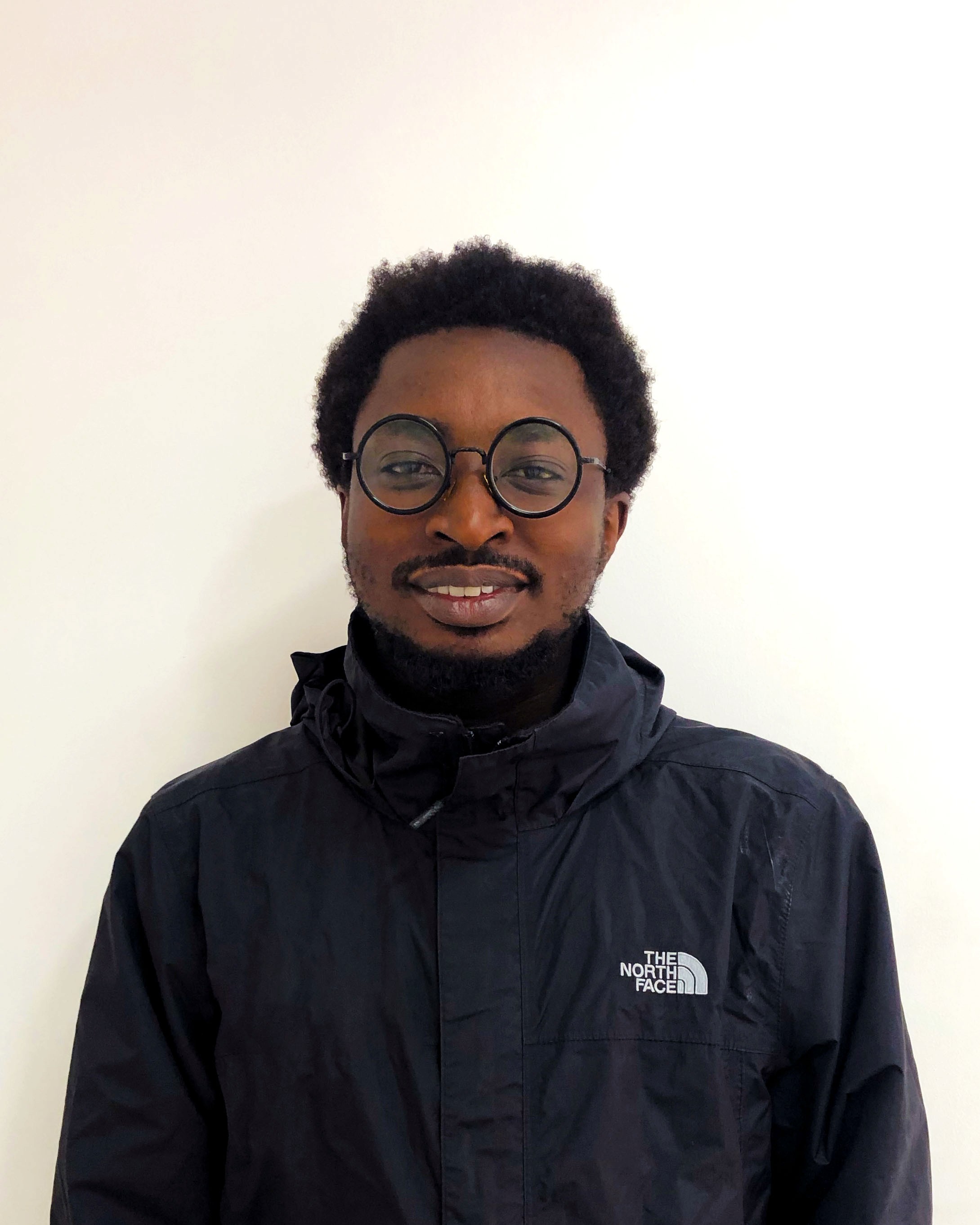 A portrait of Reuben Nyaze, a product designer, smiling warmly in a casual jacket and glasses.