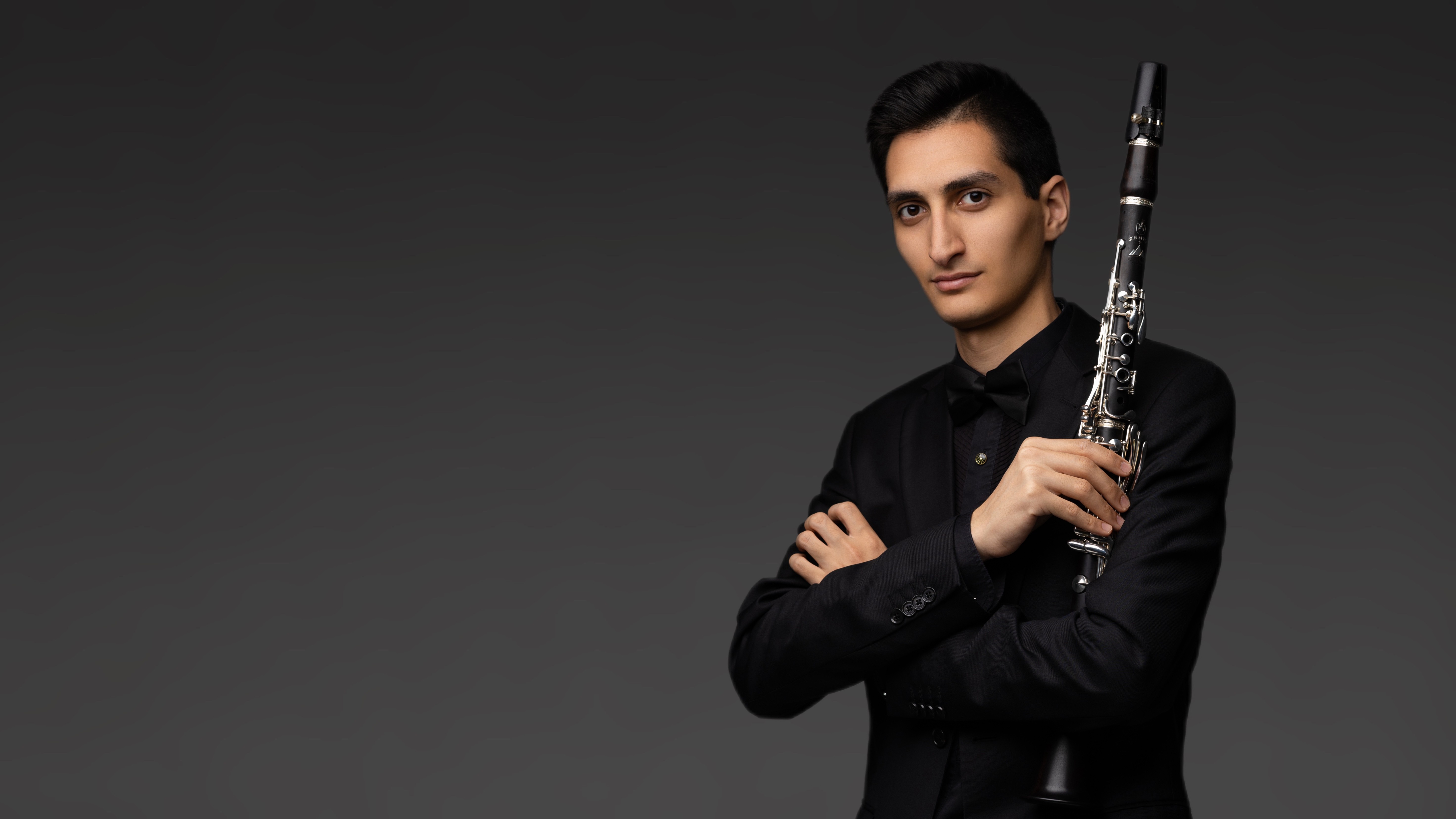     Erik Mirzoyan holding a clarinet in a dark studio portrait
