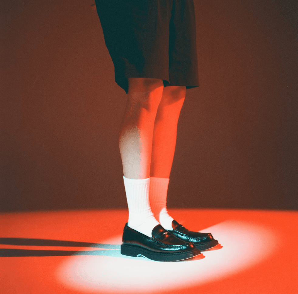 Close-up of black leather loafers worn with white socks, lit by red and blue lighting.