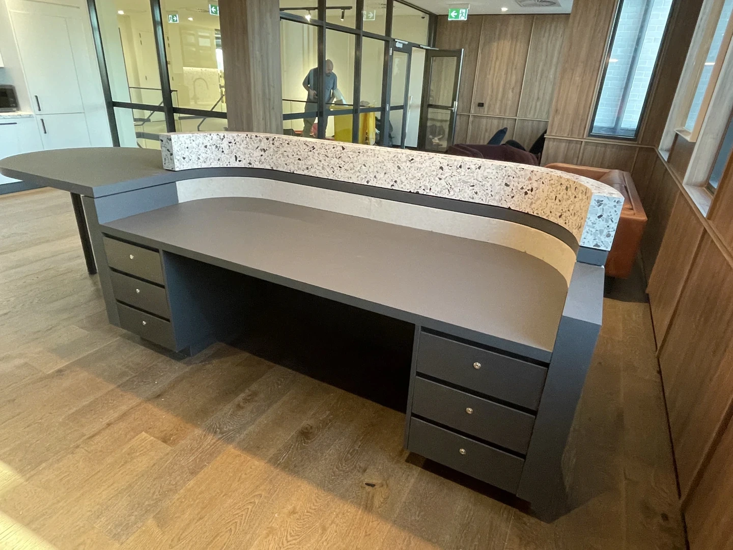 Curved terrazzo reception desk with a speckled natural stone finish, integrated drawer storage, and a sweeping counter profile for a striking commercial entrance.