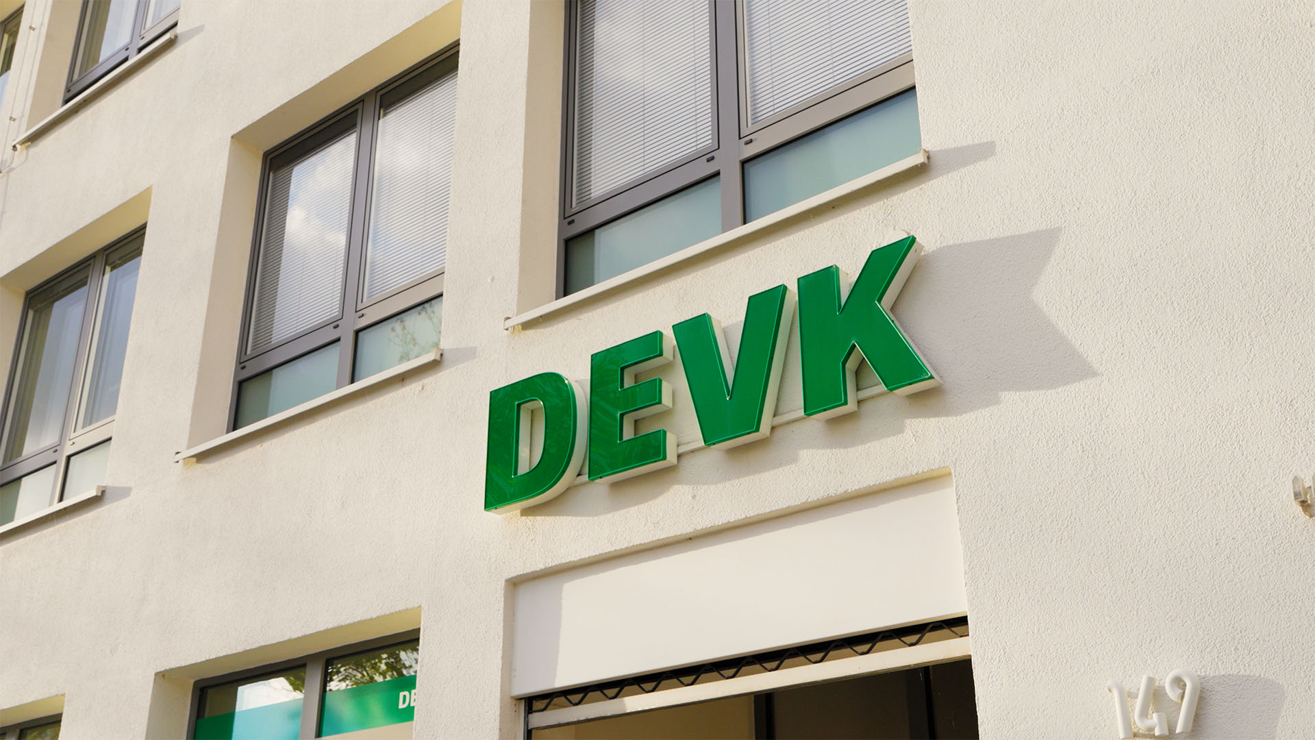 Green DEVK sign on building facade; ideal for filmproduction, advertising campaigns, and storytelling in communication.