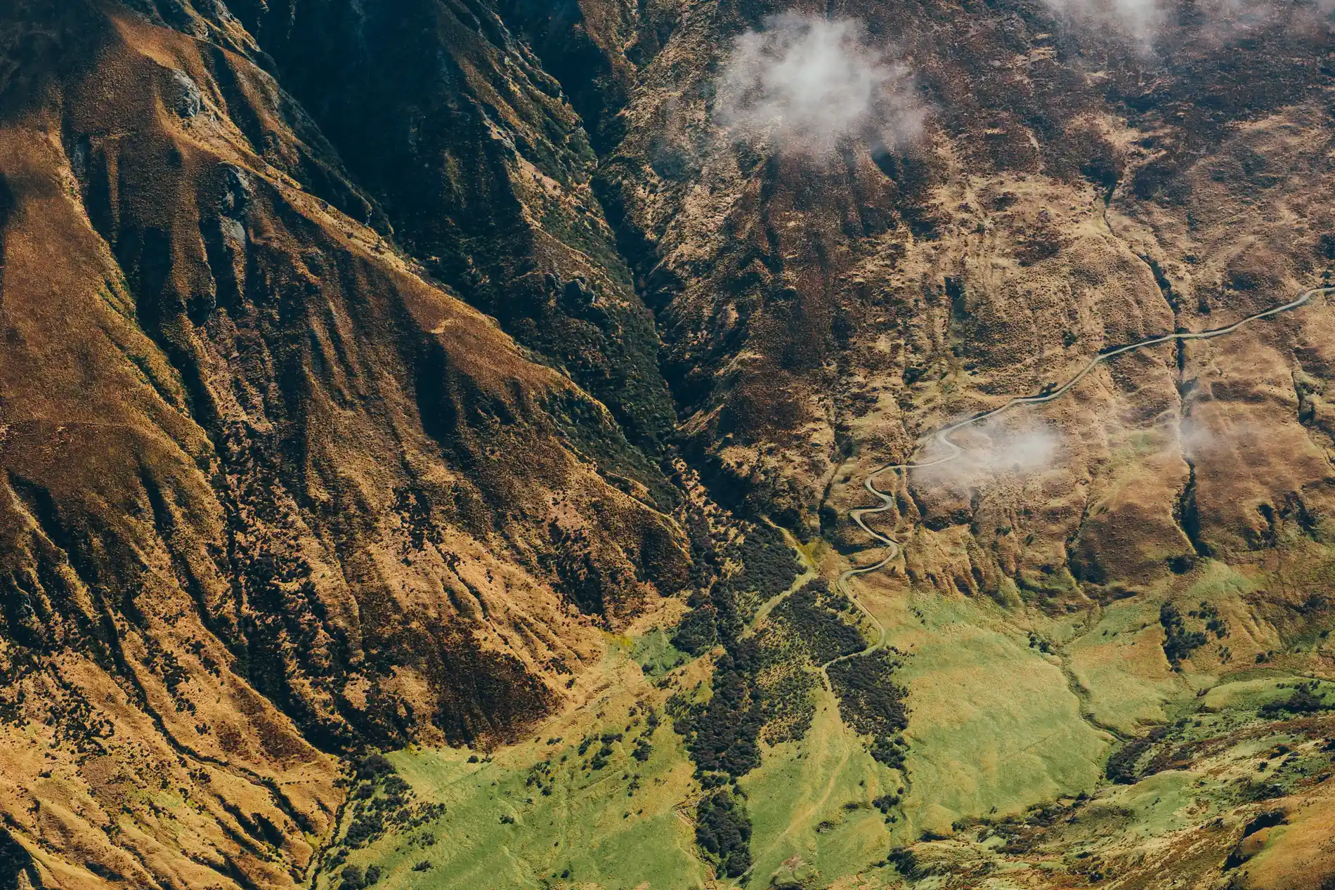 Aerial of a steep valley wall, cloud shadows moving across ochre and green slopes