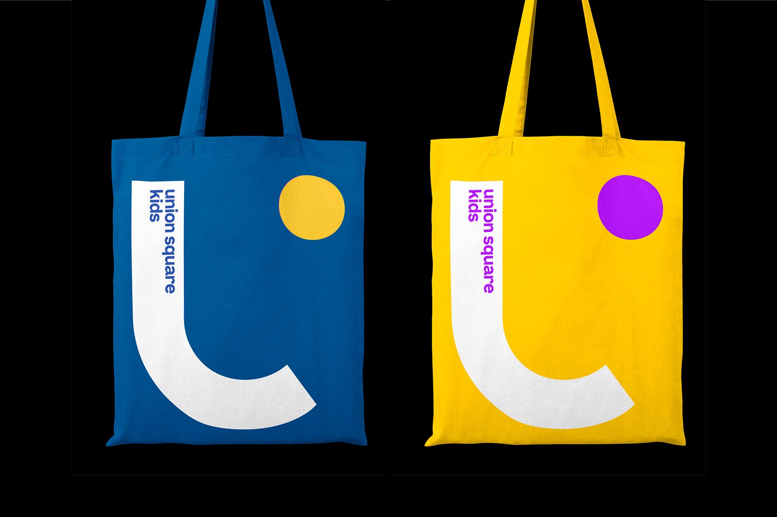 Two tote bags hang against a black background: one blue with a yellow circle, the other yellow with a purple circle.