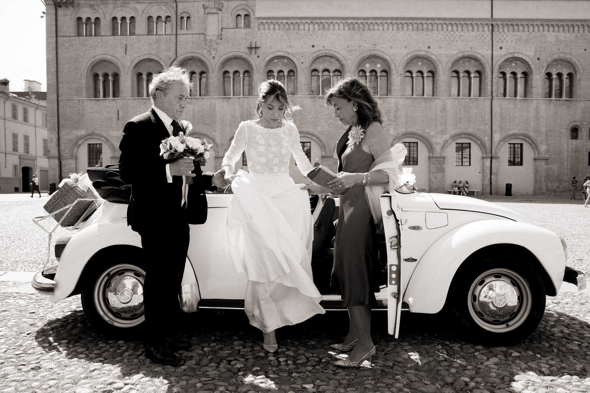 Sposi e genitori con Maggiolino bianco a Villa Peroni Riva, sposa in abito lungo, piazza in sampietrini e architettura