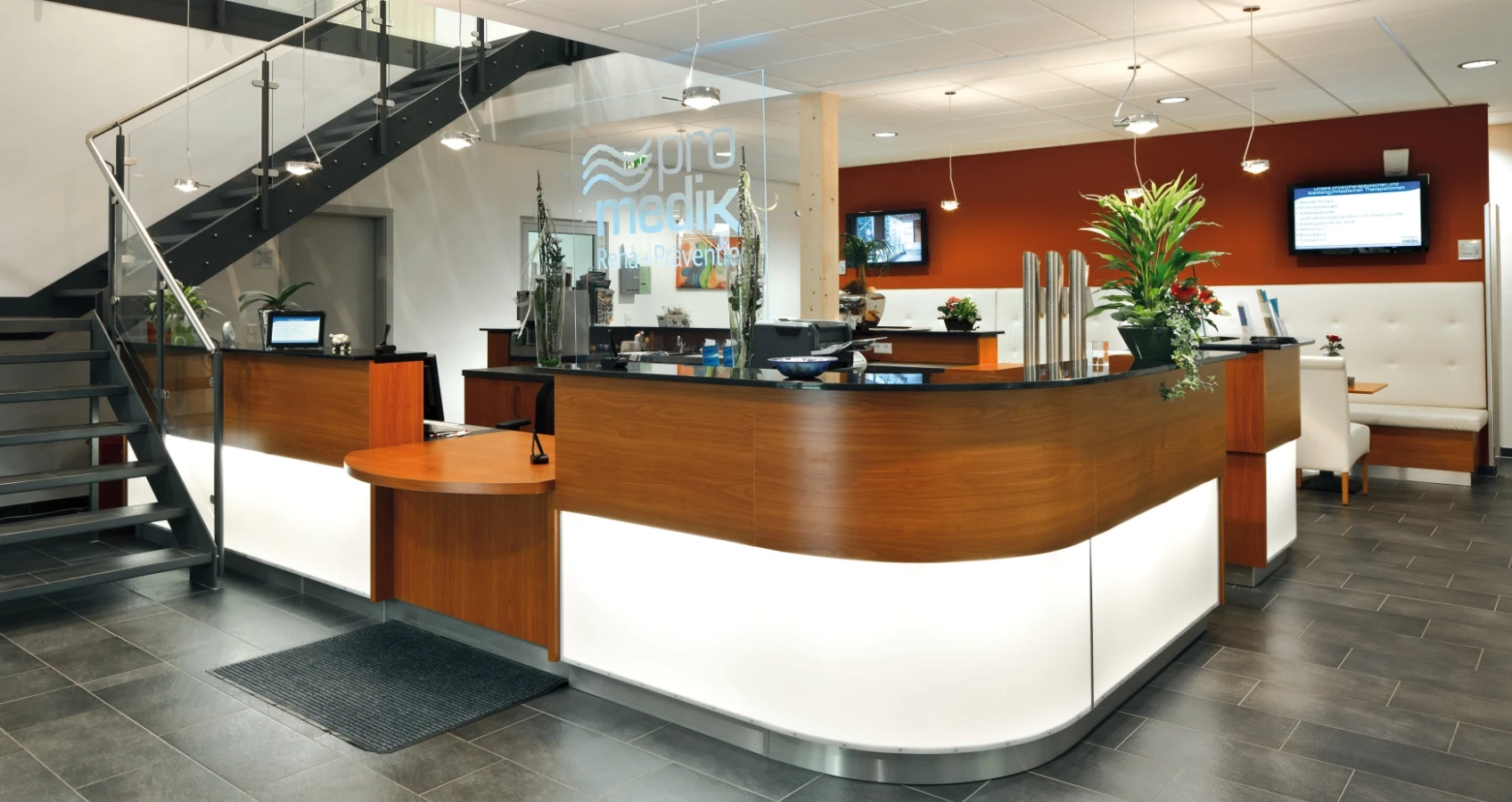 Moderne Rezeption mit Holztheke, beleuchteten Elementen und Treppe daneben.