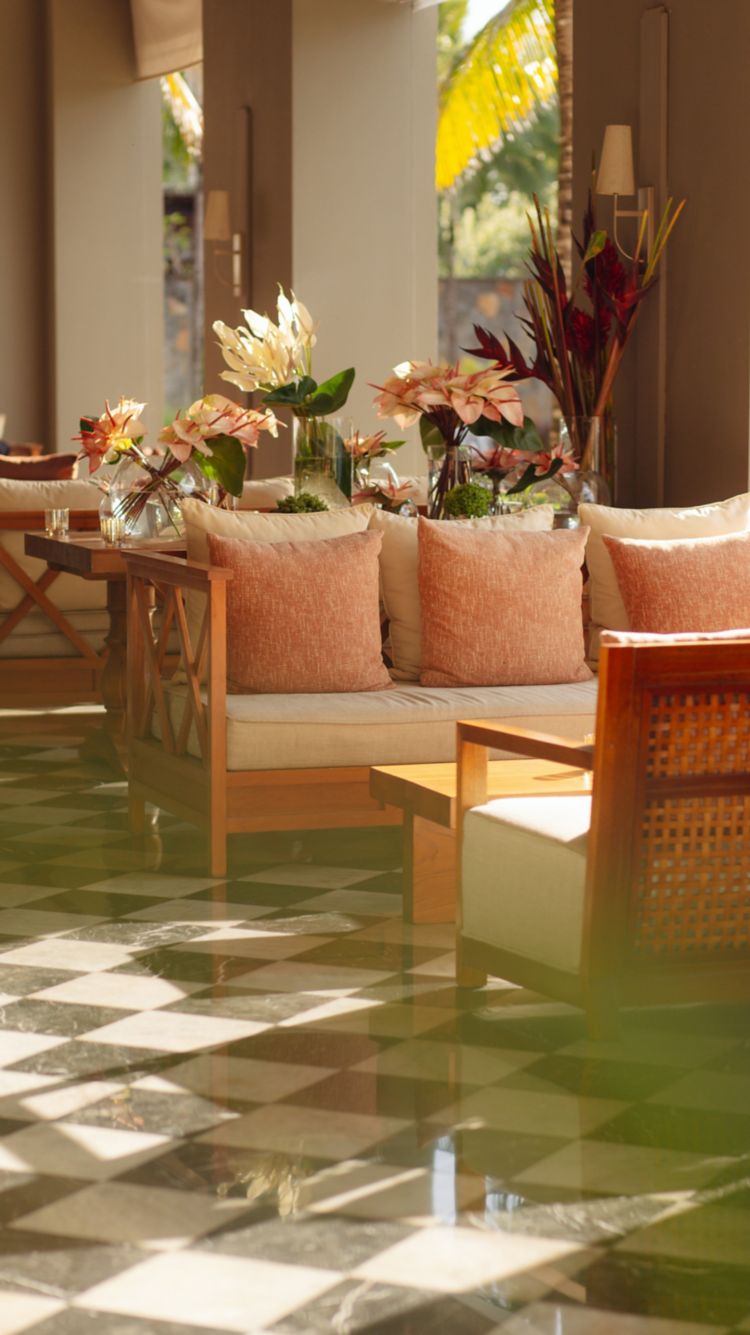 Stilvoller Loungebereich im Innenbereich mit eleganten Holzmöbeln, pfirsichfarbenen Kissen, frischen Blumenarrangements und einem klassisch schwarz-weiß karierten Marmorboden.