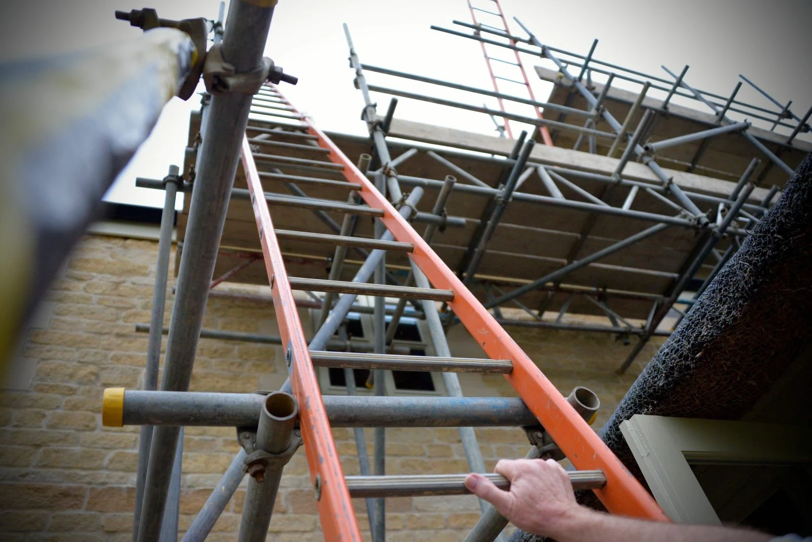 Construction worker climbing orange ladder on building site, photographed from low angle