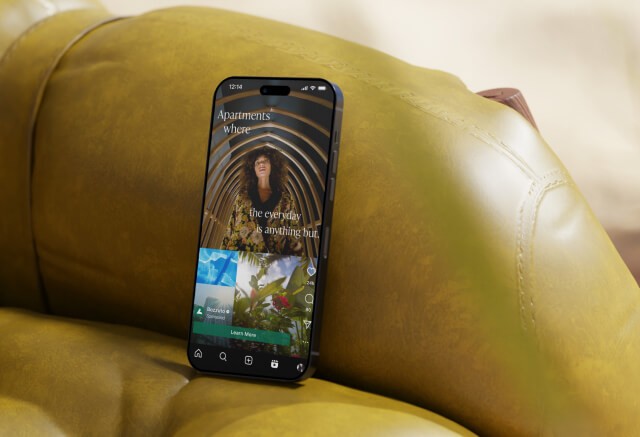 A smartphone displaying an apartment rental app screen rests upright on a yellow leather couch.
