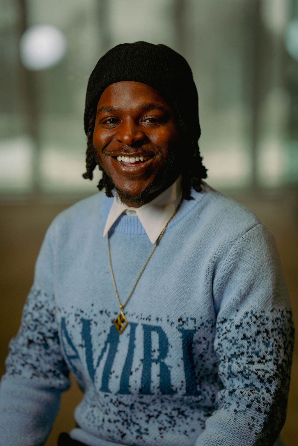 Portrait of a person with red hair, wearing a rust-colored outfit and scarf, set against a neutral gray background.
