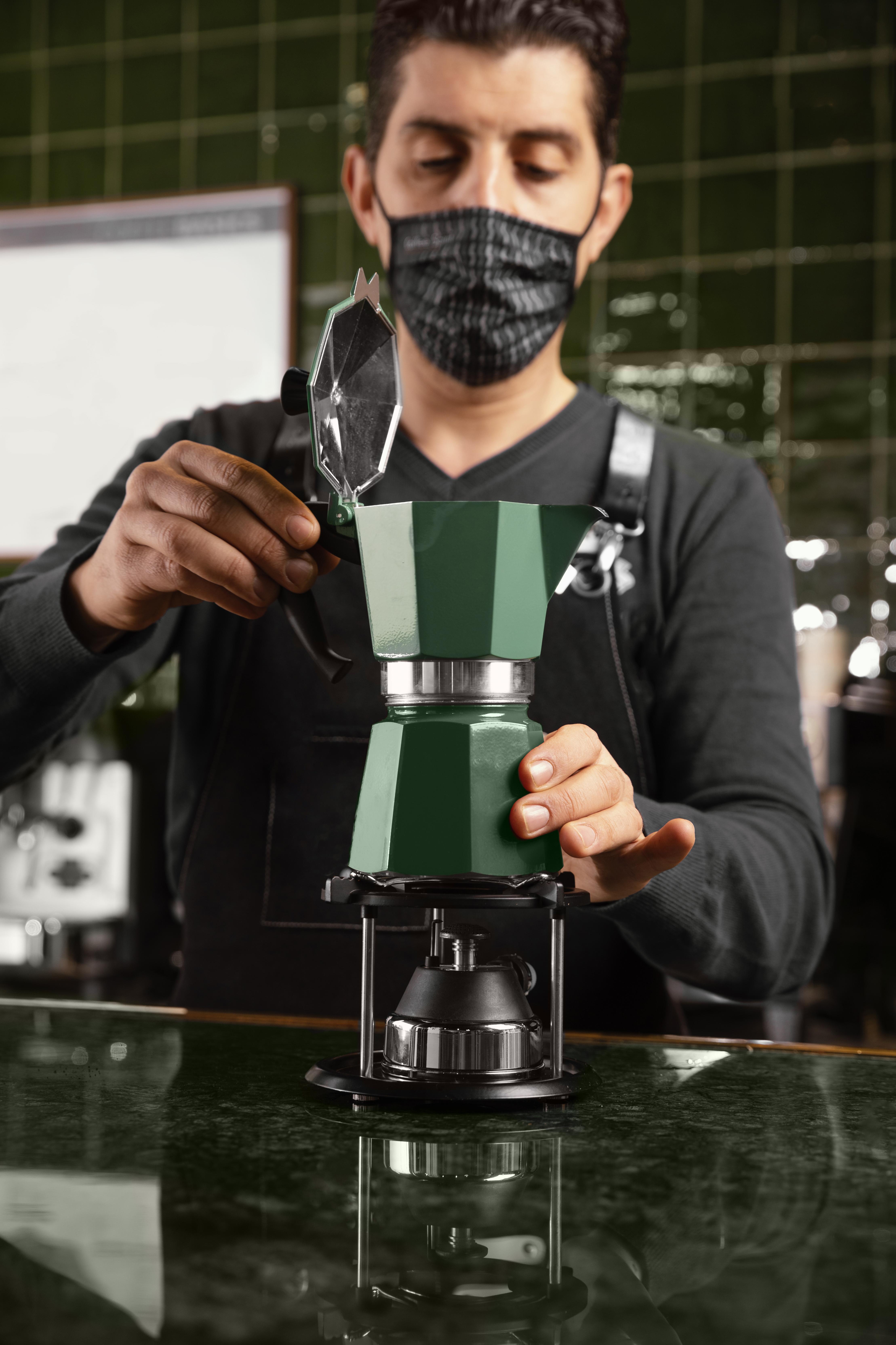 Barista in mask preparing coffee with moka pot