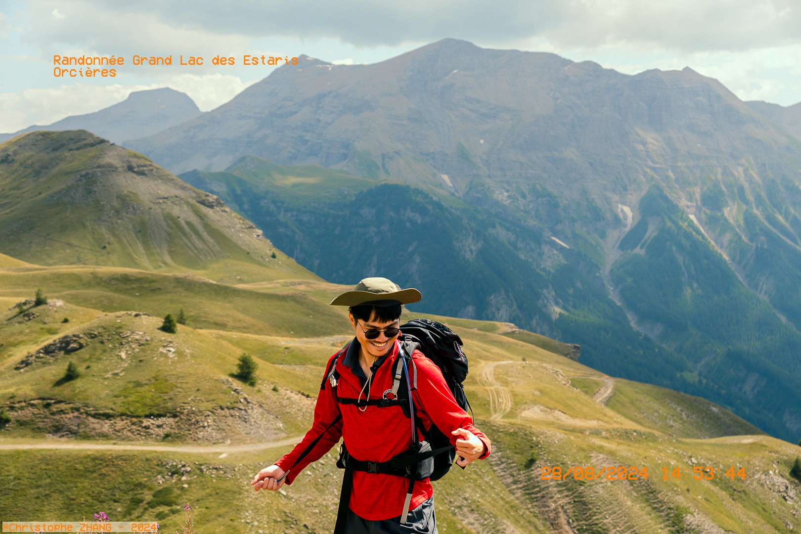 Randonneur souriant en tenue rouge sur fond de montagnes alpines.
