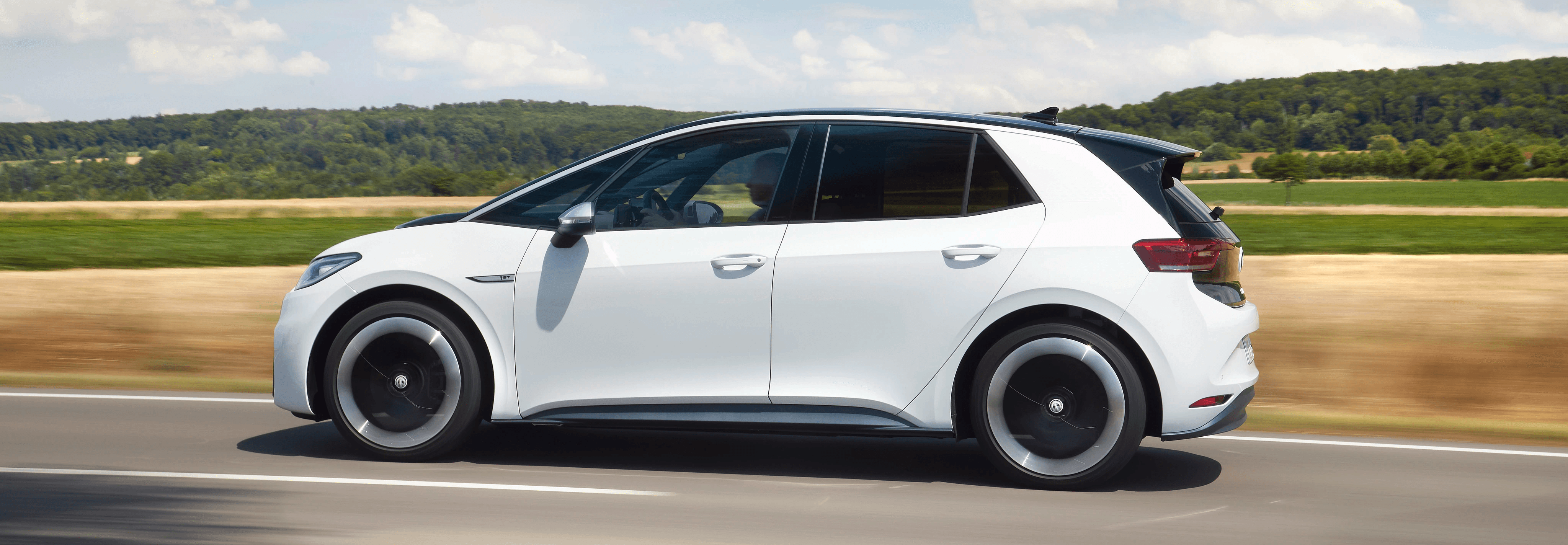 Volkswagen ID.3 blanche de profil sur route ouverte, compacte électrique en conduite dans un décor rural
