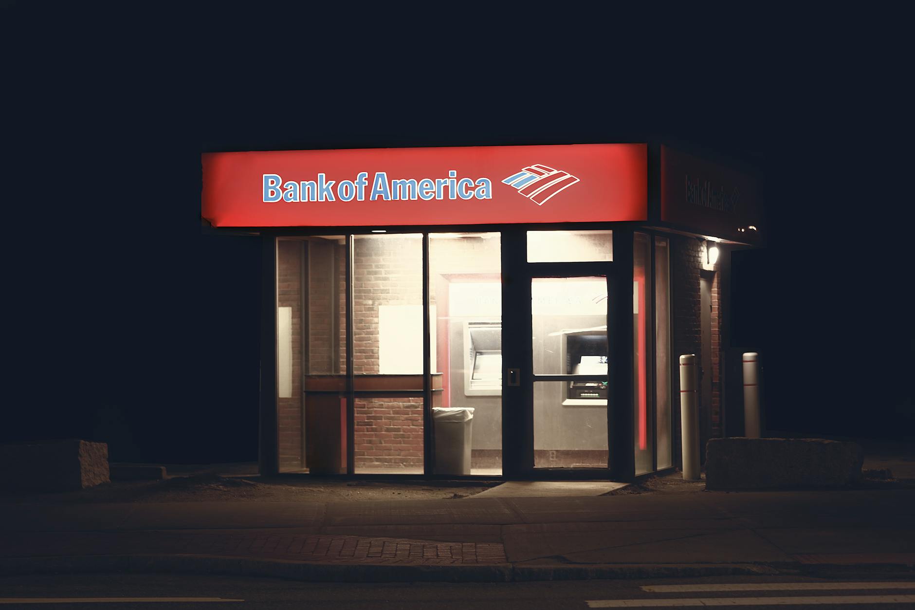 Bank of America ATM and branch exterior illuminated at night in an empty car park Financial charts and a Dow Jones values report on a clipboard on a desk with a pencil and binder clips