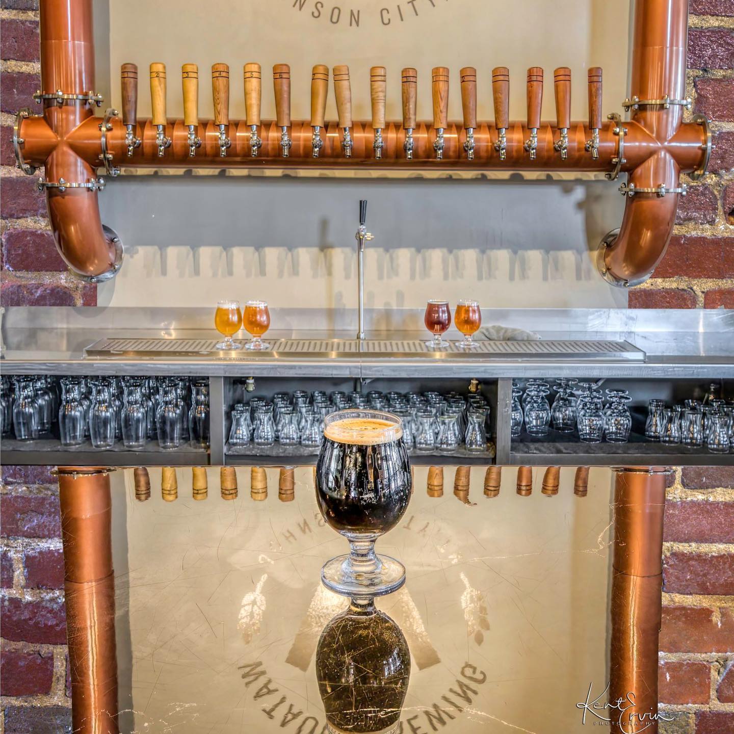 Detailed view of an ornate beer tap system with copper pipes and decorative elements against a brick background.