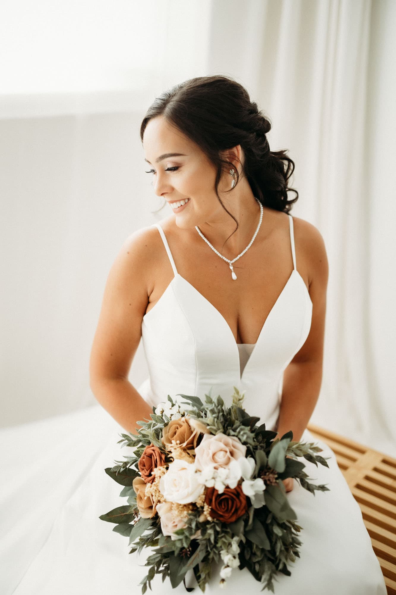 A bride in a white gown smiling off to the side, holding a floral bouquet, captured at Revelator Studio, a natural light photography studio in Shreveport.