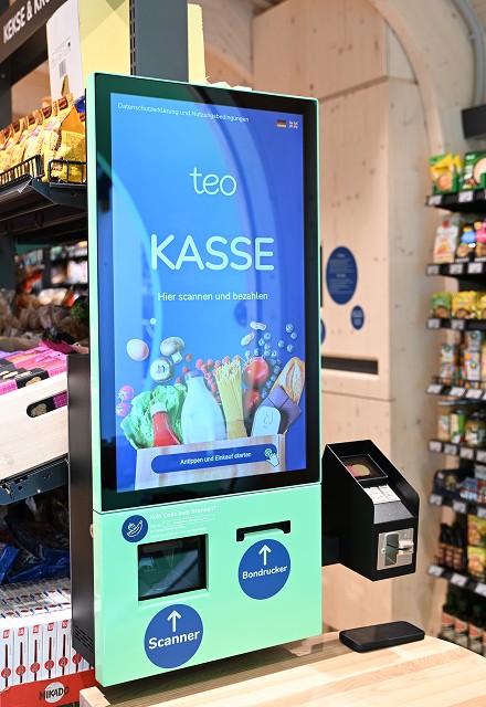 Innenansicht des neuen Smart Retail Solutions teo mit einer mintgrünen Selbstbedienungskasse im Vordergrund.