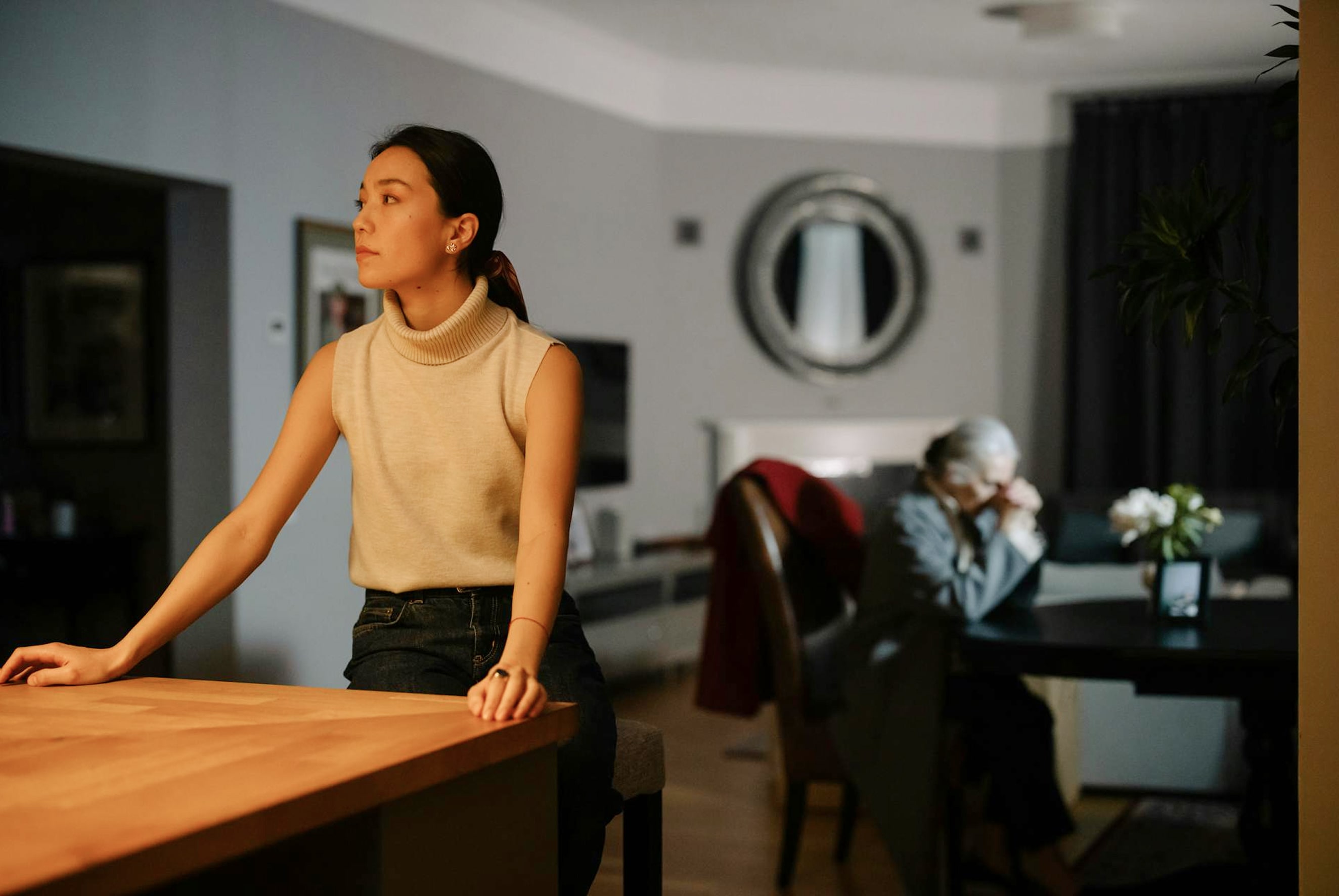 Woman standing thoughtfully in living room, representing family conflict and distance