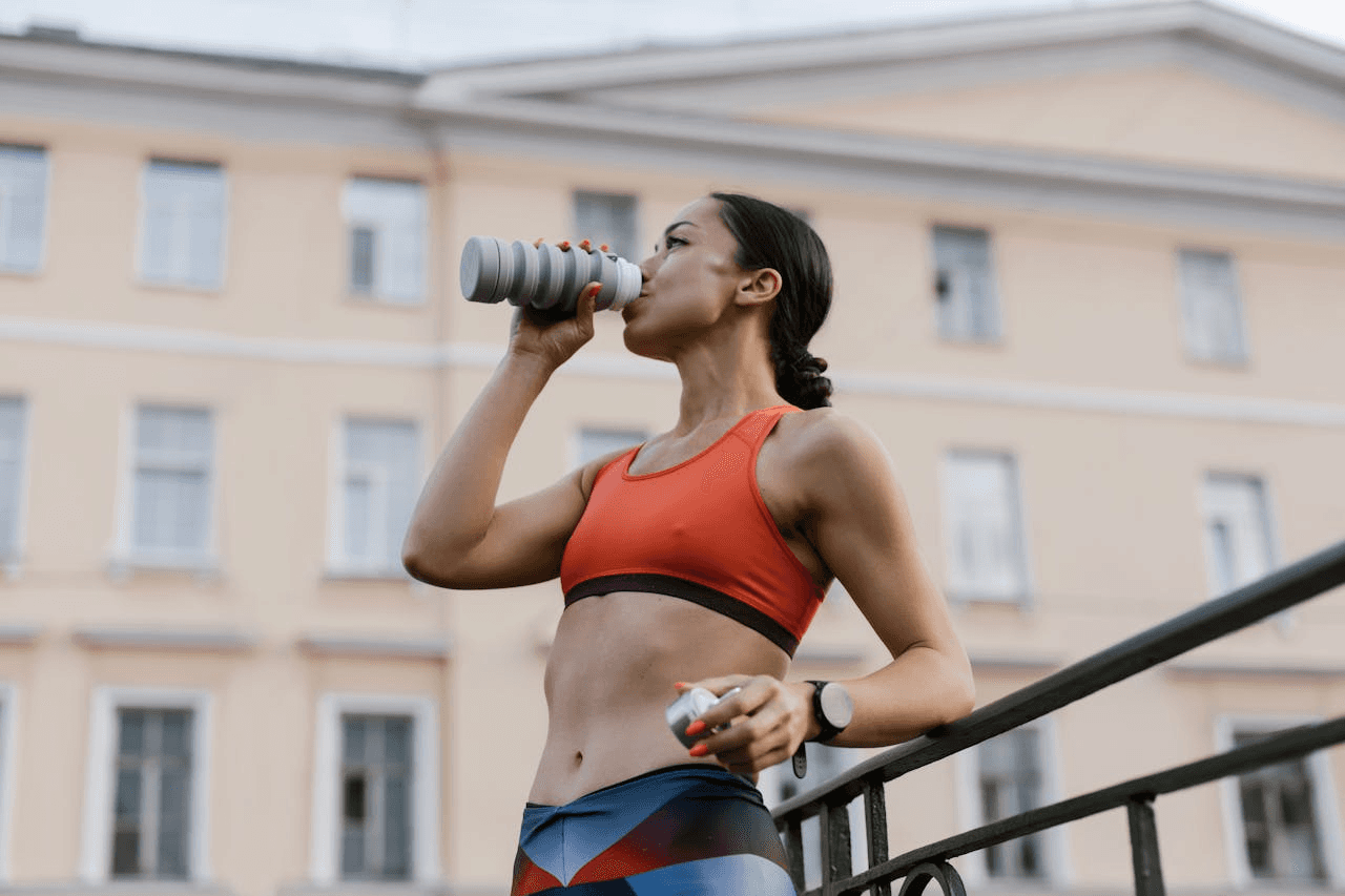 A young woman in athletic clothing takes a break from working out to drink from her water bottle.