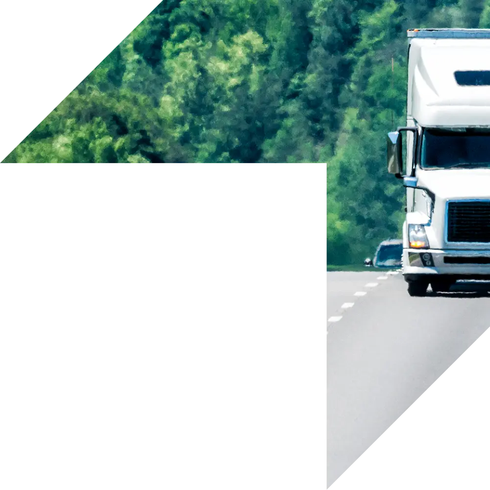 White semi-truck driving down a highway surrounded by green trees, symbolizing commercial trucking and reliable coverage.