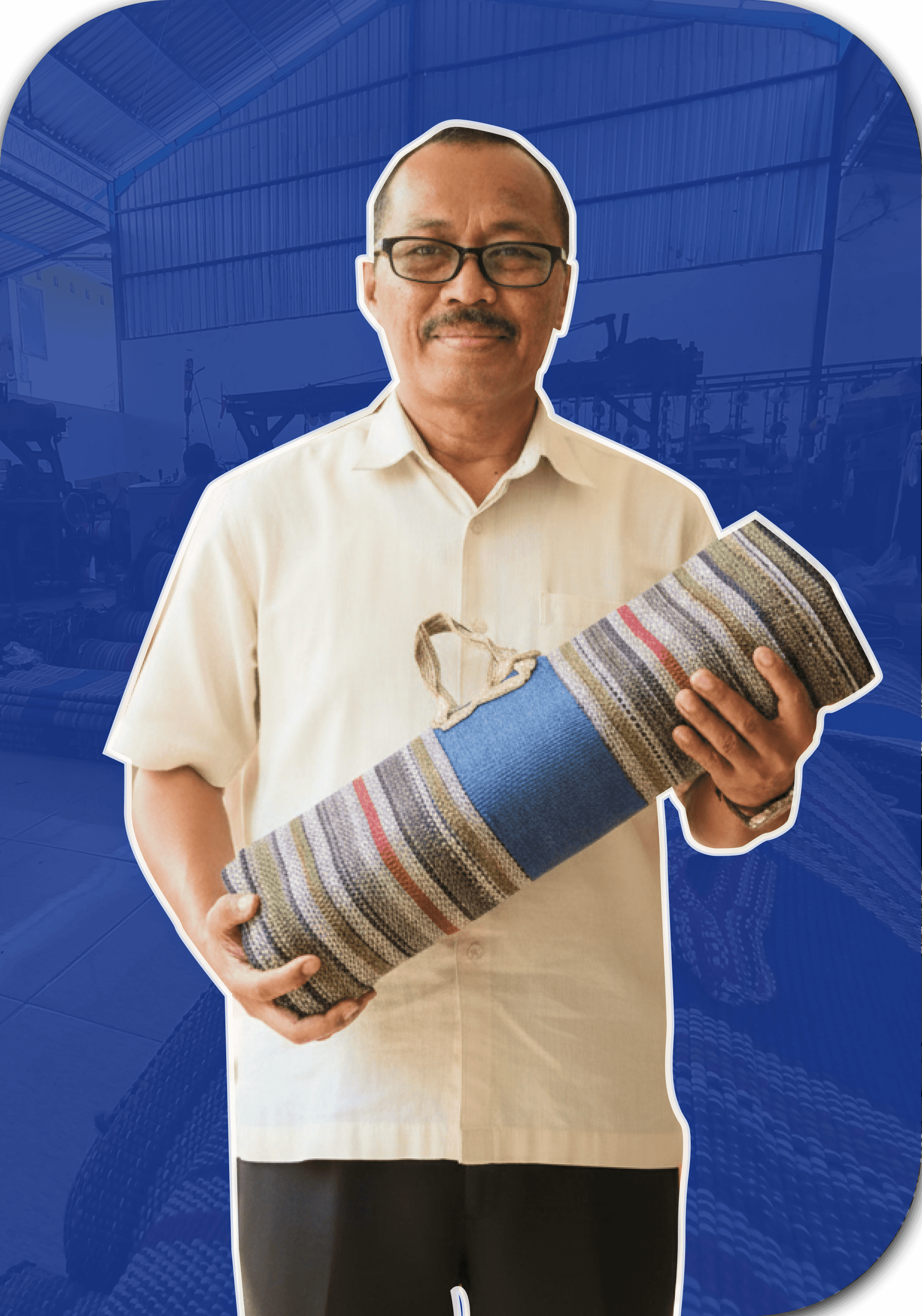 Seorang laki-laki umur sekitar 60 tahun sedang berdiri tersenyum dan menggendong tikar lipat di depanya.
