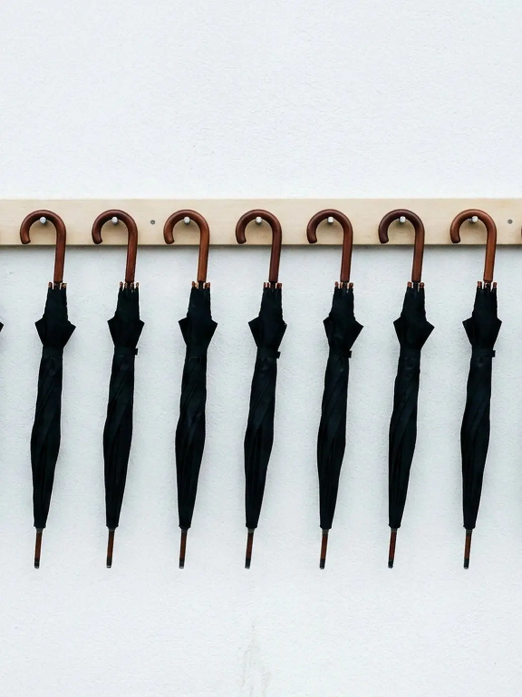 Row of black umbrellas with wooden handles on hooks