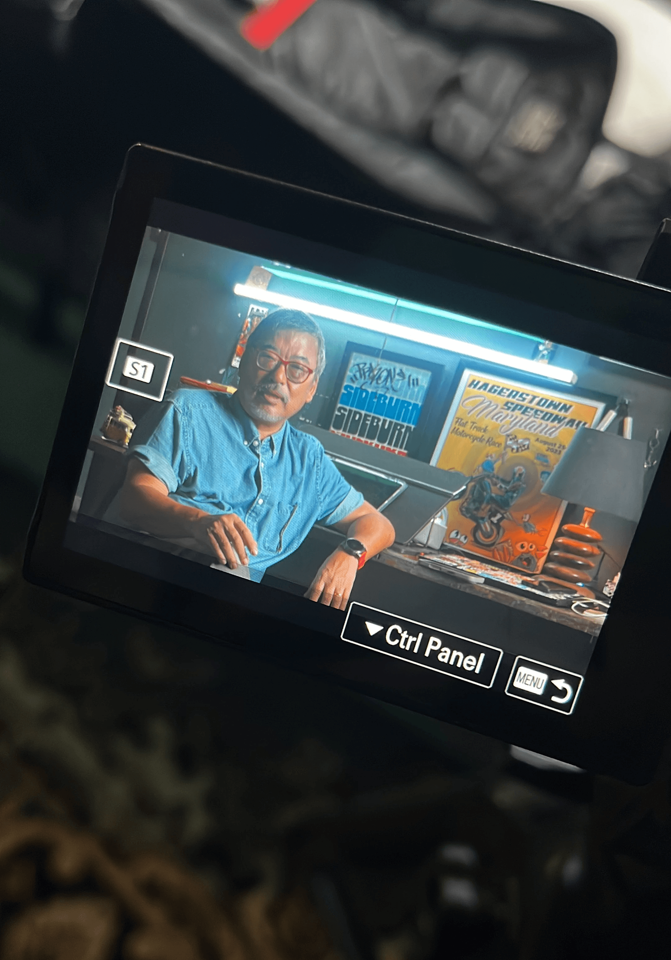 Color photo of a guitarist in a beanie playing in a rehearsal space, with bandmates blurred in the background.